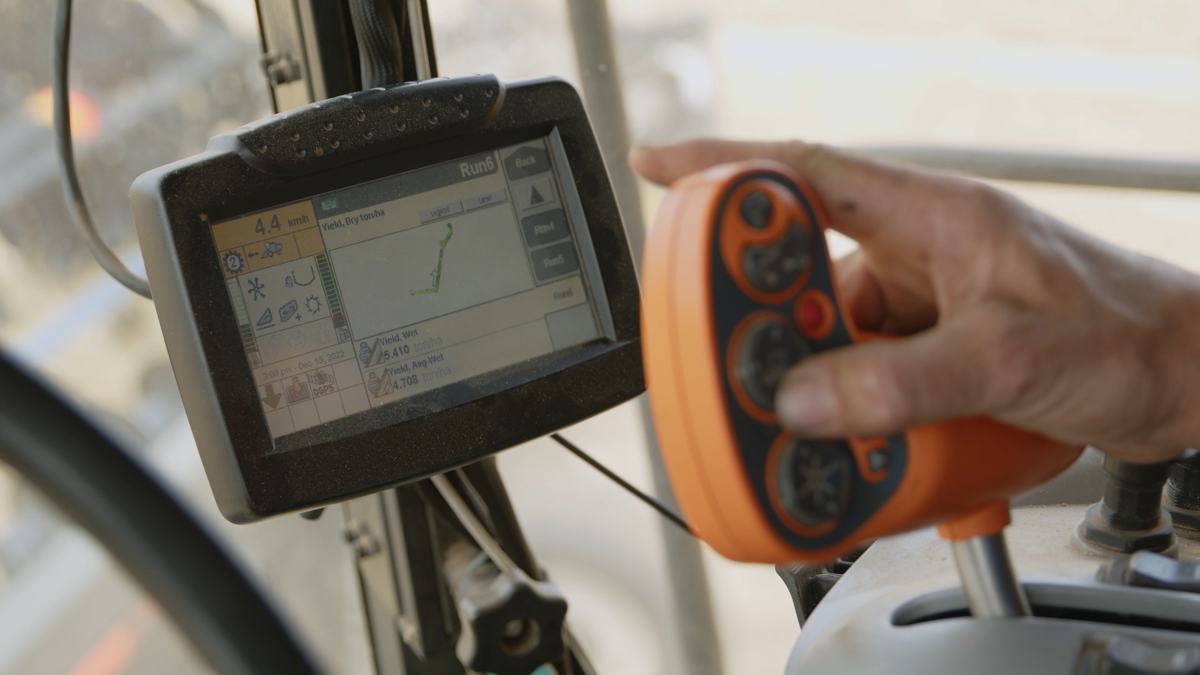A farmer's hand on the controls inside a header cab